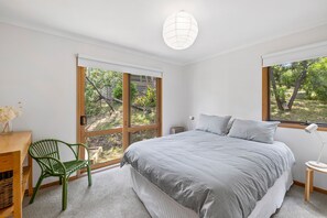 A bedroom with a large bed, a desk, a chair, and a window with a view of trees.