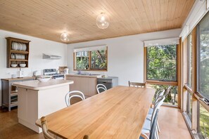 A modern kitchen with a wooden island, white cabinetry, and large windows offering a view of greenery.