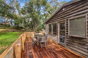 A wooden deck with a table and chairs, surrounded by a wooden fence and trees.