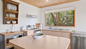 A modern kitchen with a central island, wooden cabinetry, a built-in dishwasher, and a window with a view of trees.