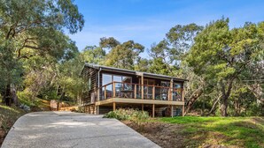 A modern wooden cabin with a deck, surrounded by trees.