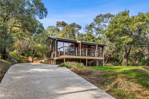 A modern wooden cabin with a deck, surrounded by trees.