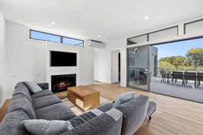Un salon moderne avec une cheminée, un canapé gris, une table basse en bois et une porte en verre donnant sur une terrasse extérieure.