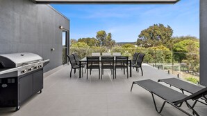 Eine überdachte Terrasse im Freien mit Grill, Esstisch, Stühlen und Liegestühlen.
