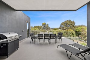 A covered outdoor patio with a grill, dining table, chairs, and lounge chairs. - Aireys Sunset Beach House (Aireys Inlet)