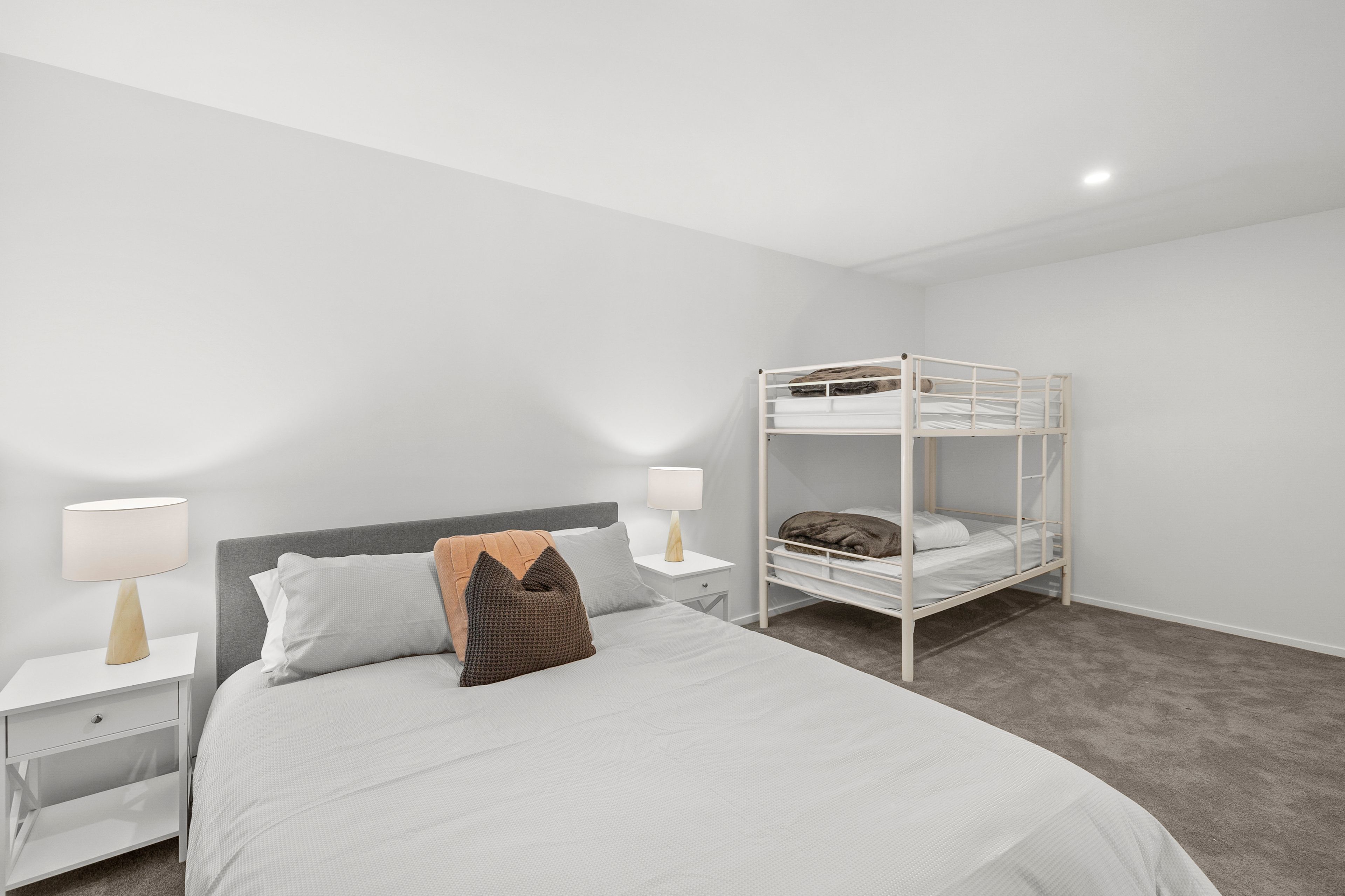 A bedroom with a bunk bed, a single bed, two bedside tables with lamps, and a grey headboard.