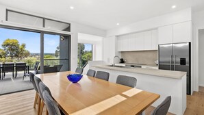 A modern kitchen with a large island, stainless steel appliances, and a dining area with a wooden table and chairs. - Aireys Sunset Beach House (Aireys Inlet)