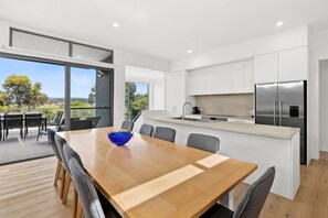 A modern kitchen with a large island, stainless steel appliances, and a dining area with a wooden table and chairs. - Aireys Sunset Beach House (Aireys Inlet)
