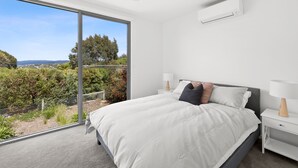 Ein Schlafzimmer mit großem Fenster, einem Bett mit Kissen, einem Nachttisch und einem Deckenventilator.