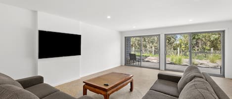A modern living room with a flat-screen TV, a wooden coffee table, and grey upholstered sofas.