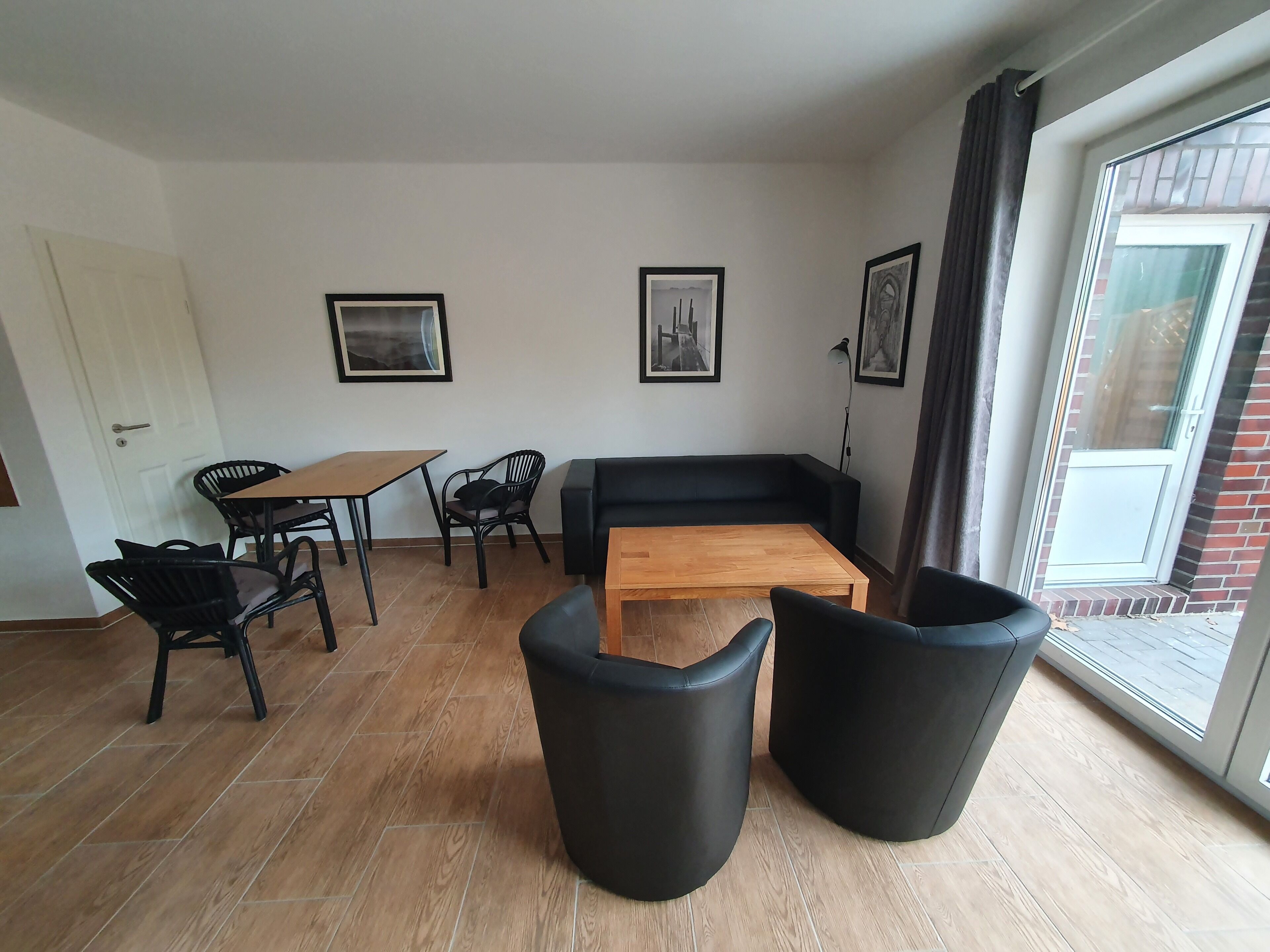 A modern living room with a sofa, coffee table, and black chairs. There are framed pictures on the wall and a door to the left.