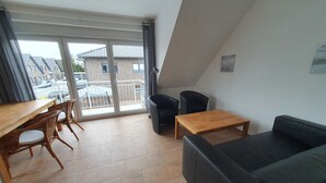 A modern living room with a wooden dining table, two black chairs, a black sofa, and a small wooden coffee table. - Haus Taybeerweg (Aurich)