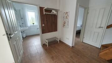 A hallway with a wooden floor, a radiator, a drying rack, and a door leading to a bathroom.
