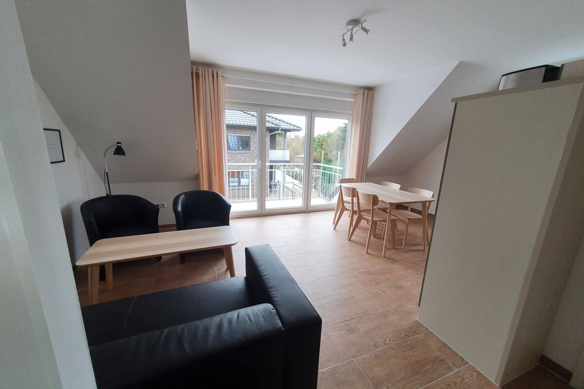 A modern living space with a sofa, a dining table with chairs, a lamp, and a large window with curtains.