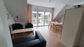 En moderne stue med sofa, spisebord med stole, lampe og et stort vindue med gardiner.