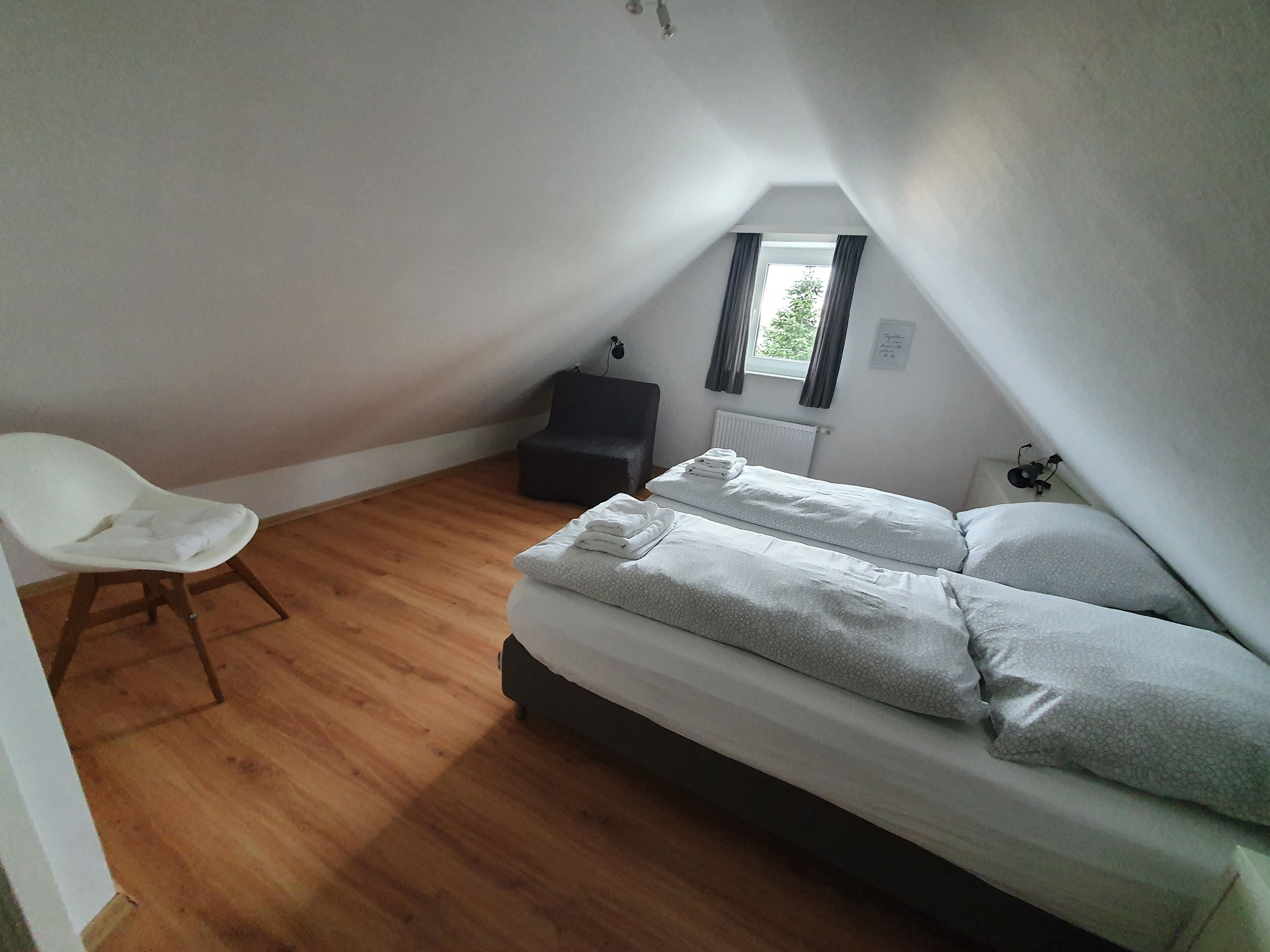 Une petite pièce propre, avec un lit simple, une chaise et une fenêtre.