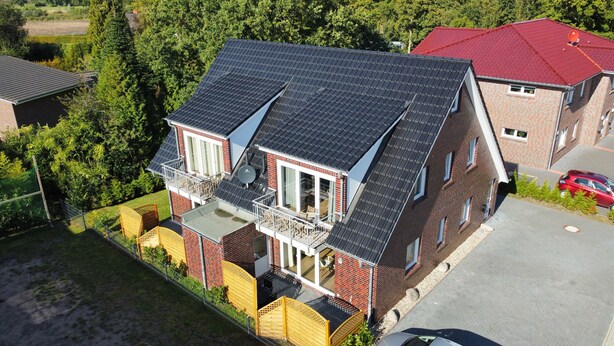 A two-story house with a sloped roof, a balcony, and a fenced backyard. - Haus Taybeerweg (Aurich)