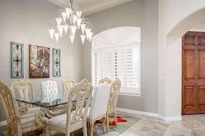 A dining area with ornate chairs, a glass table, a chandelier, and artwork on the wall. - Camelback Corridor, 5 min from Airport, Pool & Sun (Phoenix)