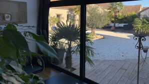 En vy genom ett fönster ut mot en innergård med en palmpalm, en liten trädgård och en byggnad med ett tak täckt av tegelpannor.