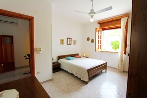 Ein Schlafzimmer mit einem Bett, einem Holz-Kopfteil, Nachttischen, einem Deckenventilator und einem Fenster mit Vorhängen.