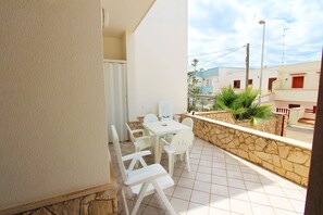 Ein Balkon mit einem weißen Tisch und Stühlen, einer Steinmauer und Blick auf benachbarte Gebäude.