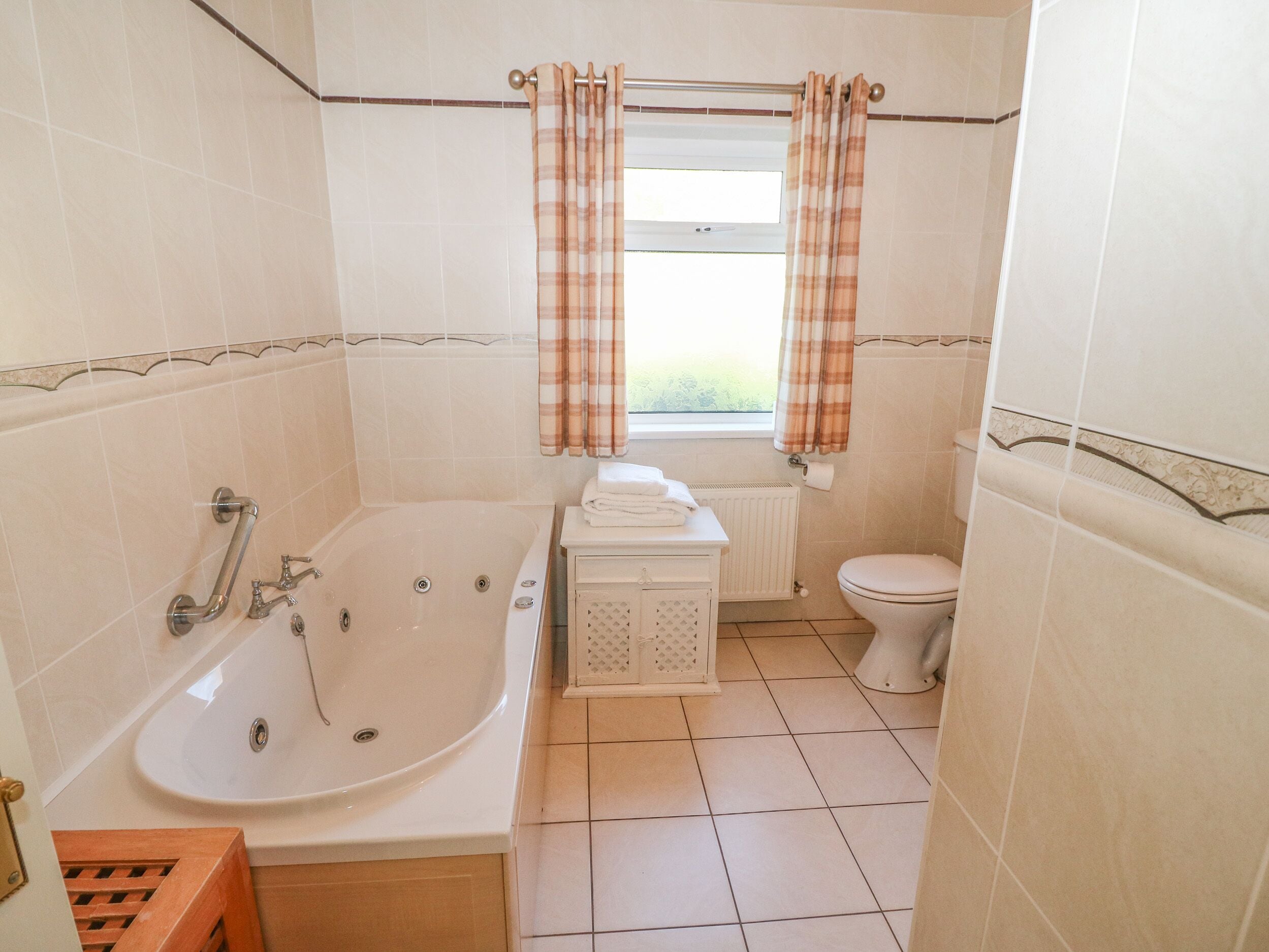 A bathroom with a bathtub, toilet, and a window with curtains.