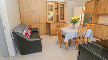 A compact kitchen with wooden cabinets, a dining table with chairs, a black sofa, and a refrigerator.