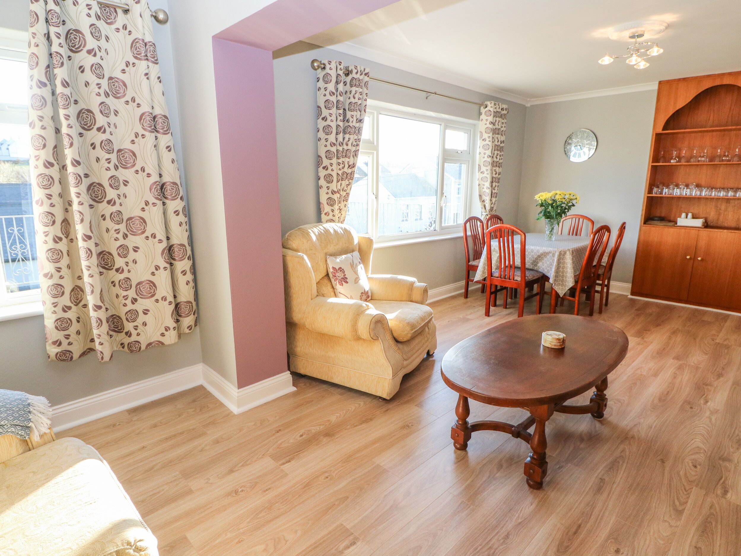 A cozy living room with a sofa, a dining table with chairs, a wooden cabinet, and a window with curtains.