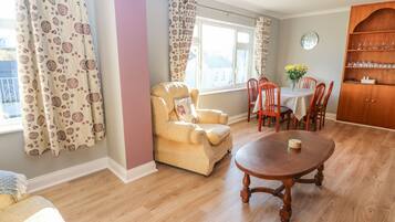 A cozy living room with a sofa, a dining table with chairs, a wooden cabinet, and a window with curtains.