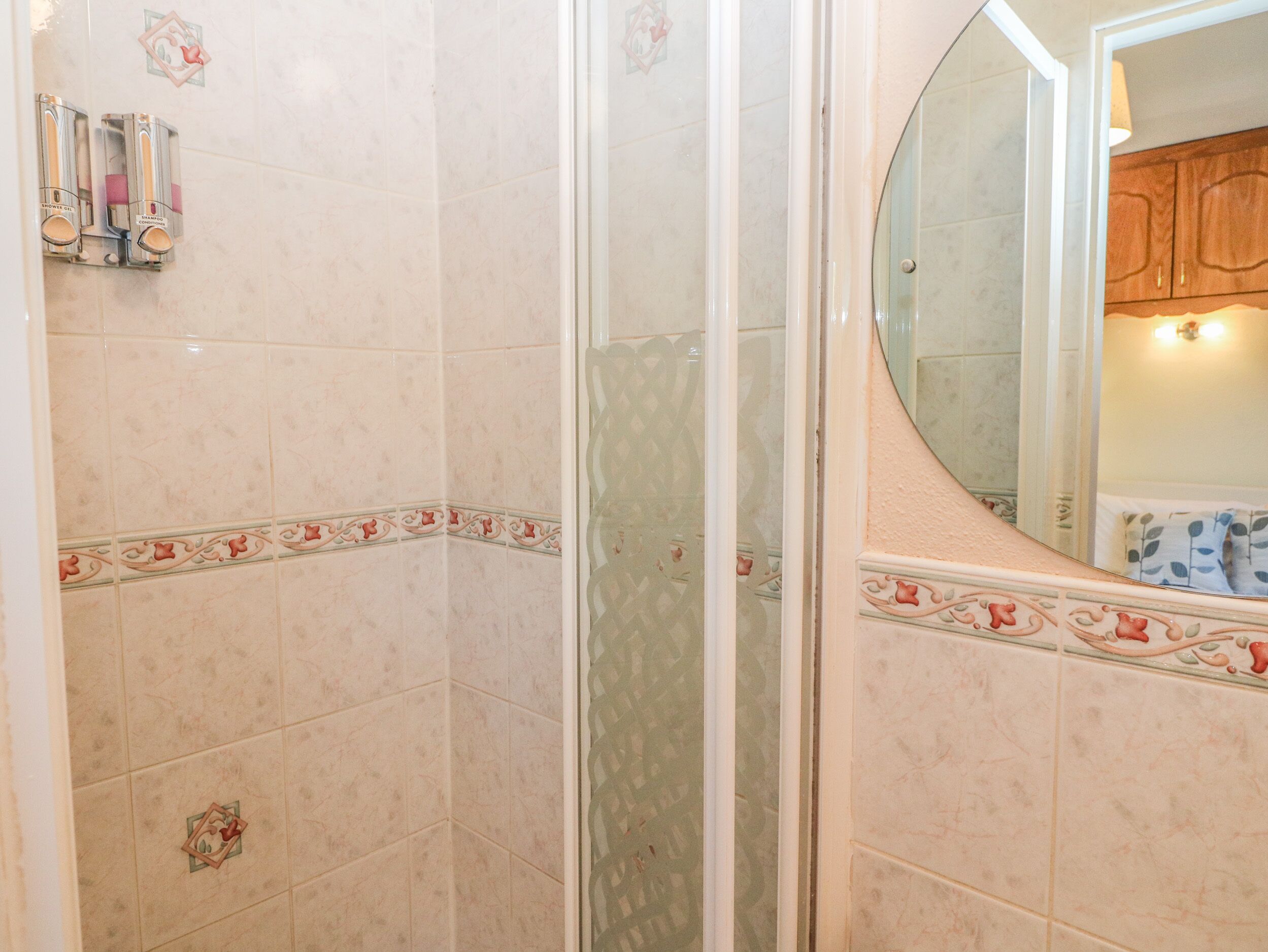 Un baño con zona de ducha, paredes con azulejos y un espejo.
