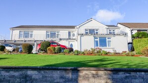 A two-story house with a white exterior, a red car parked in the driveway, and a well-maintained lawn. - Lavender Cottage (Castletownbere)