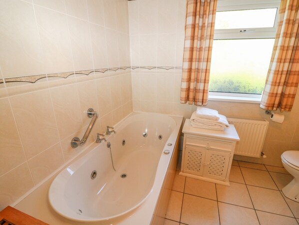 Un baño con bañera, inodoro y una ventana con cortinas.