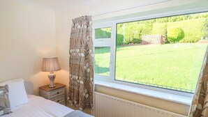 A bedroom with a bed, a bedside table with a lamp, a window with a view of a lawn and fence. - Lavender Cottage (Castletownbere)