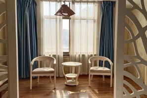 Una habitación con suelo de madera, una mesa redonda blanca, dos sillas blancas y cortinas azules.