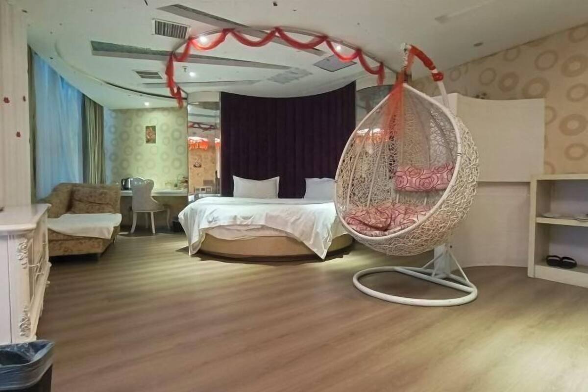 A bedroom with a bed, a hanging chair, a desk, and a chair.