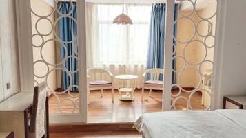 Un dormitorio con una cama, un escritorio y una silla. Se ve una ventana con cortinas y una lámpara colgante.