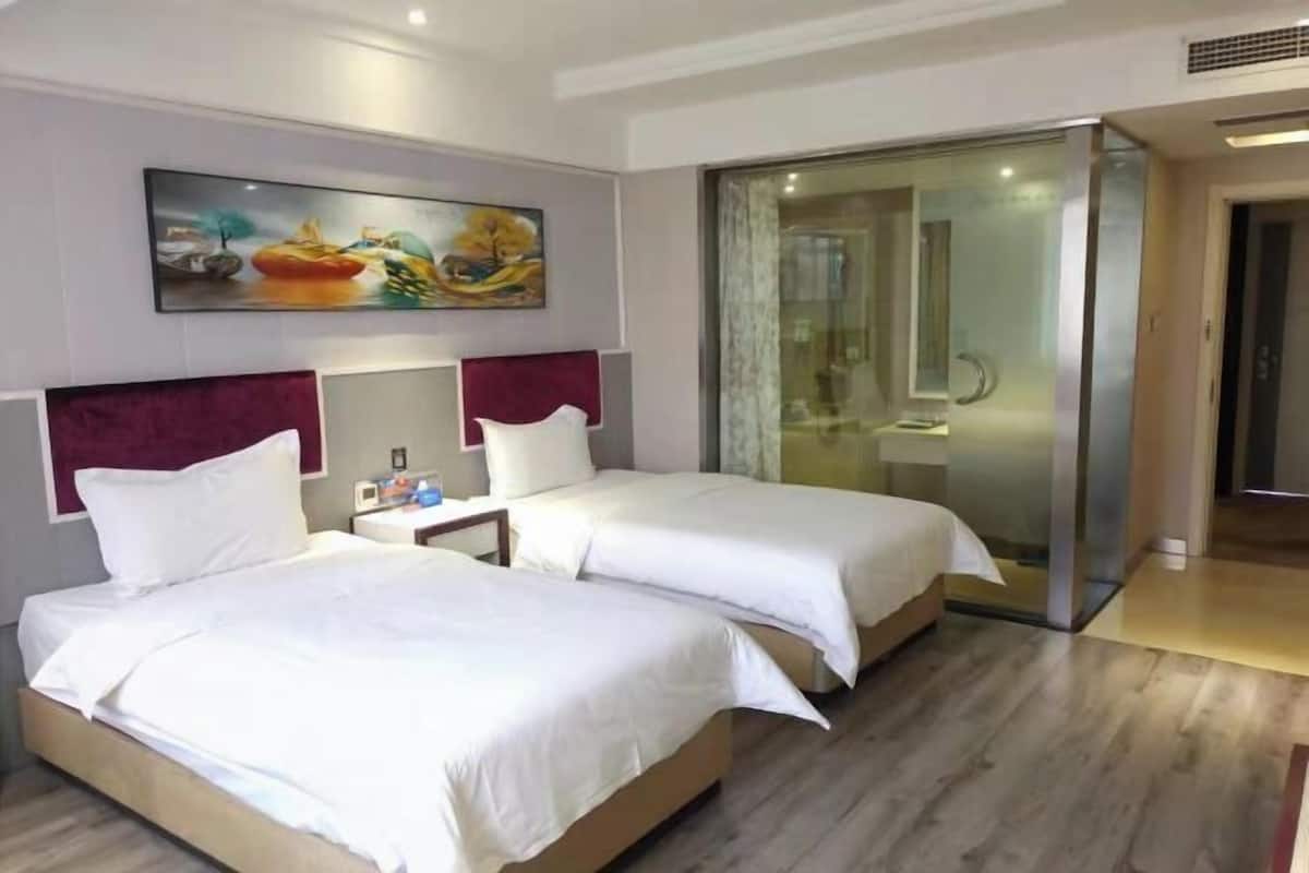 A hotel room with two beds, a painting on the wall, and a sliding glass door leading to a bathroom.