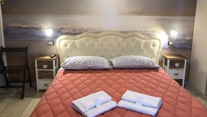 Un dormitorio con cama, dos mesitas de noche, una silla y un mural en la pared que representa un cielo nublado sobre el agua.