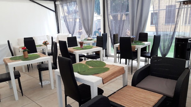 Un restaurante con mesas de mimbre blanco y sillas negras, hojas verdes en los centros de mesa y vistas al exterior a través de amplias ventanas.
