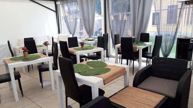 Un restaurante con mesas de mimbre blanco y sillas negras, hojas verdes en los centros de mesa y vistas al exterior a través de amplias ventanas.