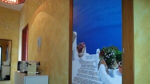 A hallway with a white cabinet, a wooden door, and a wall with a painted view of white buildings and blue sky. - B b Oasis Passion Fiera - Triple Room With Wifi and Ac, External Bathroom (Rho)