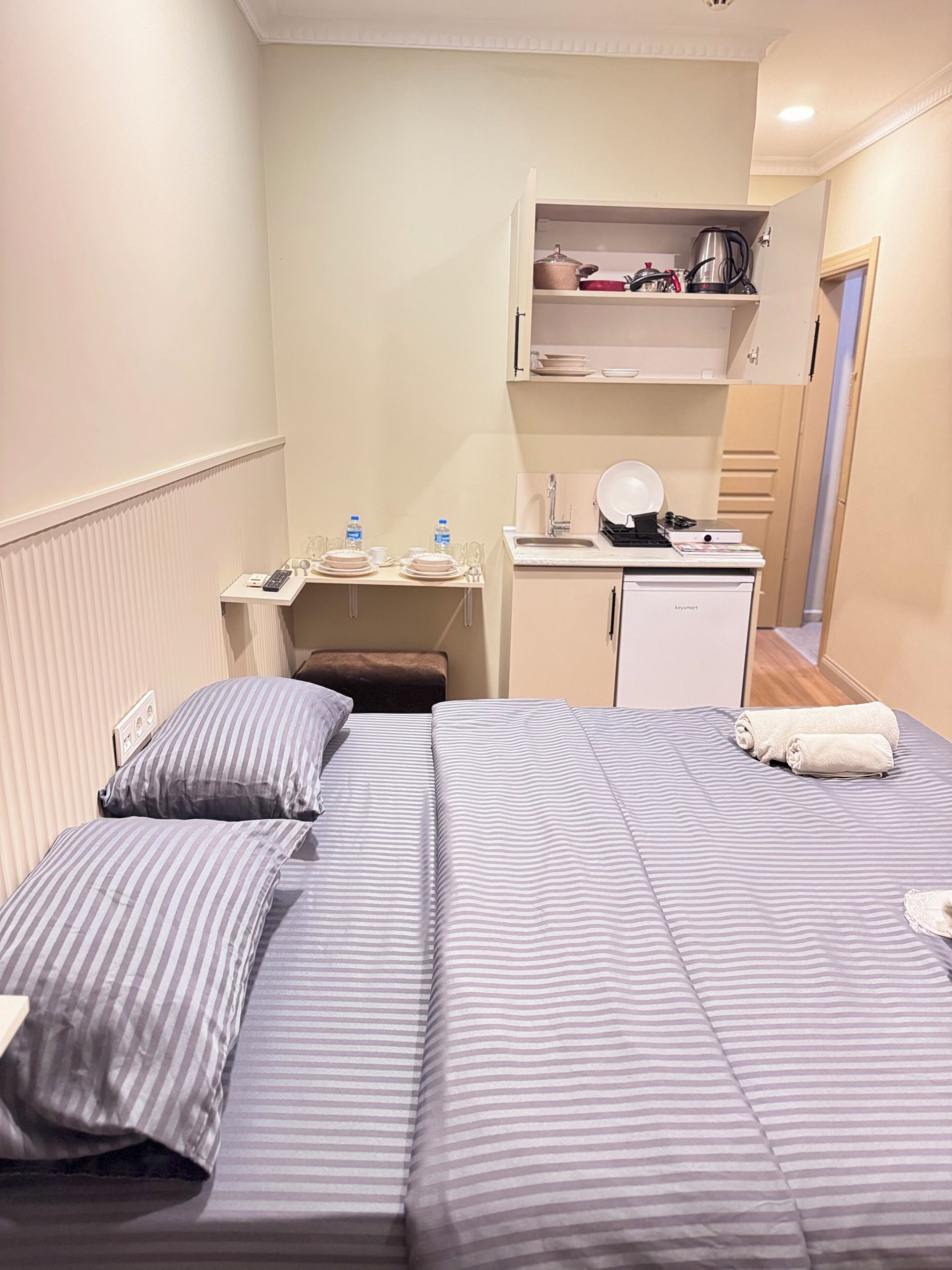 A hotel room with a bed, bedside table, a small kitchenette, and a bathroom.