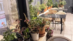 Un interior moderno con plantas en macetas, una mesa negra, sillas de mimbre y un gran ventanal.