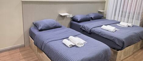 Quarto de hotel com duas camas, piso de madeira, radiador e janela com cortinas.