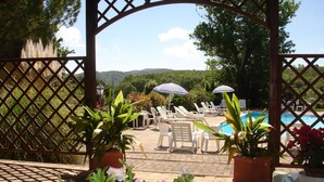 Un área junto a la piscina con sillones de descanso y sombrillas, rodeada de plantas y flores en macetas.