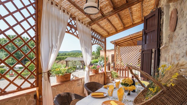 Una terraza con mobiliario de mimbre, una mesa lista para comer y plantas en macetas.