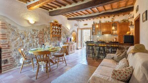 Un interior rústico con paredes de piedra vista, vigas de madera, un comedor con mesa y sillas, un sofá y armarios de cocina.