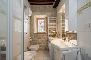A compact bathroom with a stone wall, a white sink, a toilet, and a shower area. - Superior Ground Floor Apartment With Pool View (Casole d'Elsa)