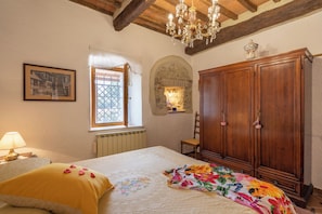 A bedroom with a bed, a wooden wardrobe, a chandelier, a window with curtains, and a framed picture on the wall. - Superior Ground Floor Apartment With Pool View (Casole d'Elsa)