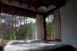 Um quarto com uma cama, uma janela com cortinas e vista para árvores.